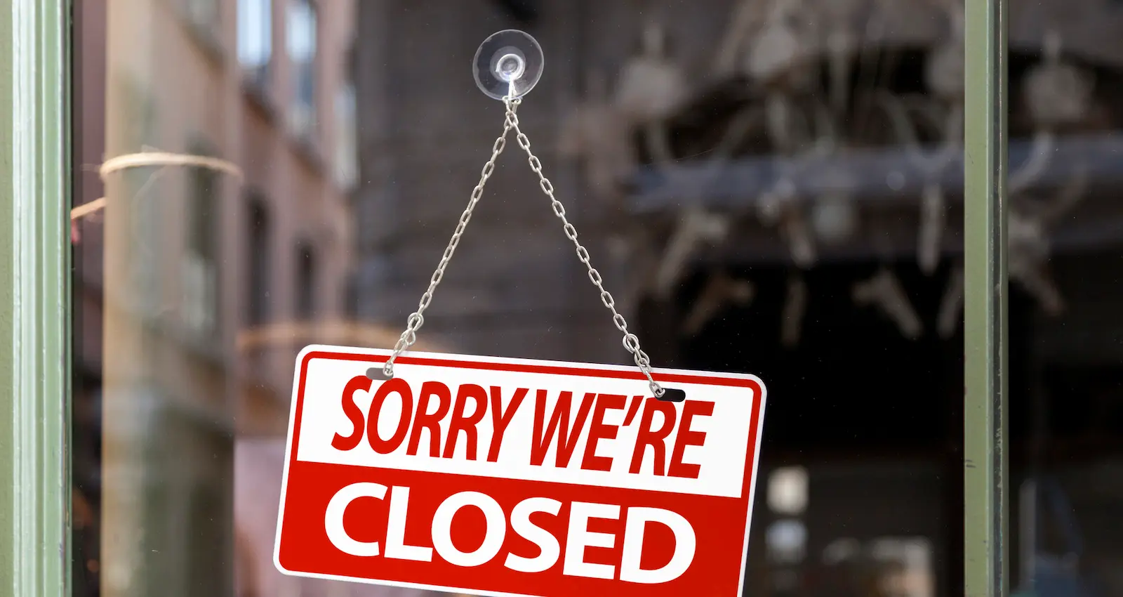 Rotes Hinweisschild mit der Aufschrift „Sorry we’re closed“ an einer Glastür eines Geschäfts