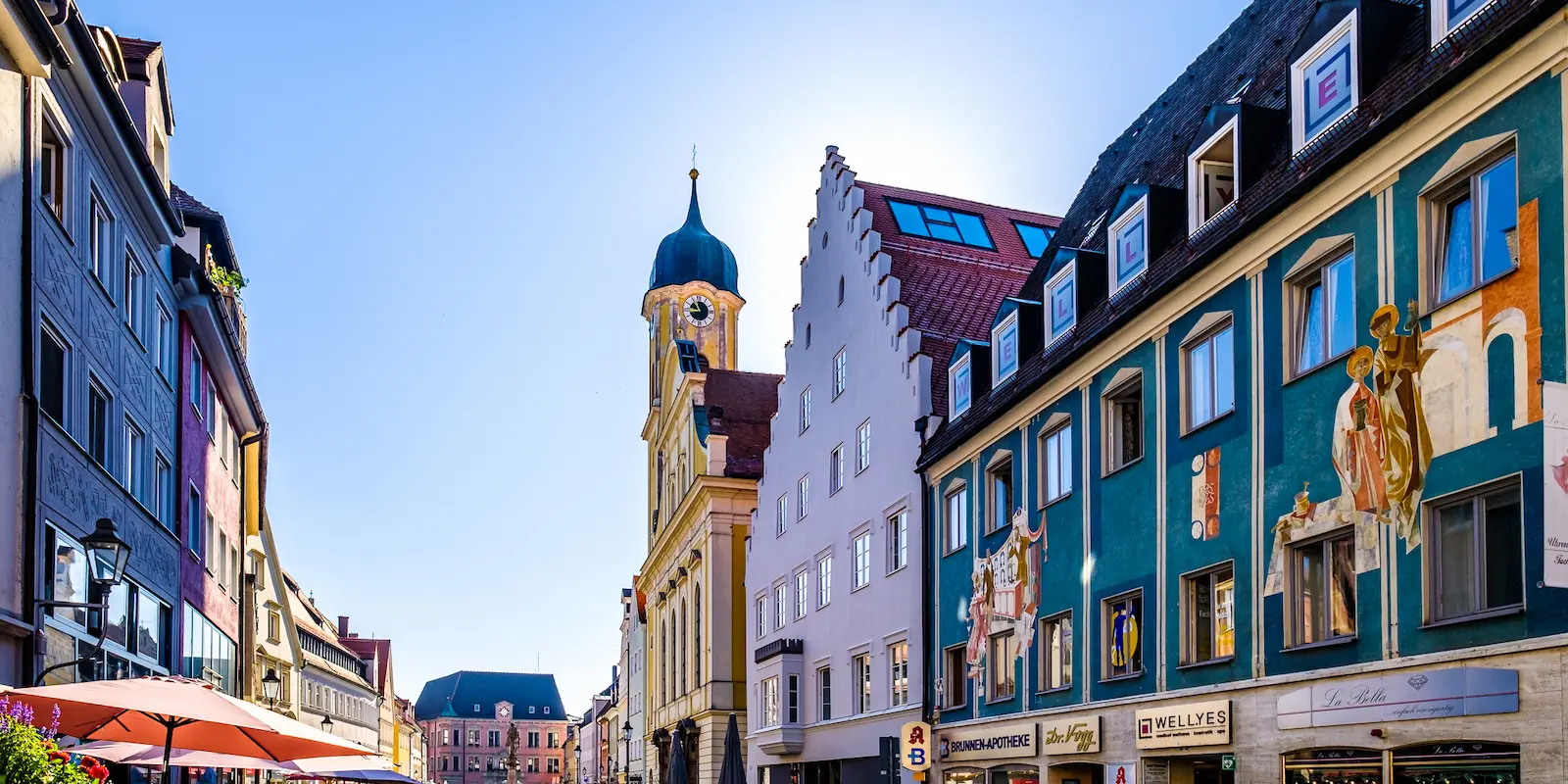 Blick in die Altstadt von Kaufbeuren mit bunten Fassaden, Lüftlmalerei und barocker Kirche bei klarem Himmel und Sonnenschein