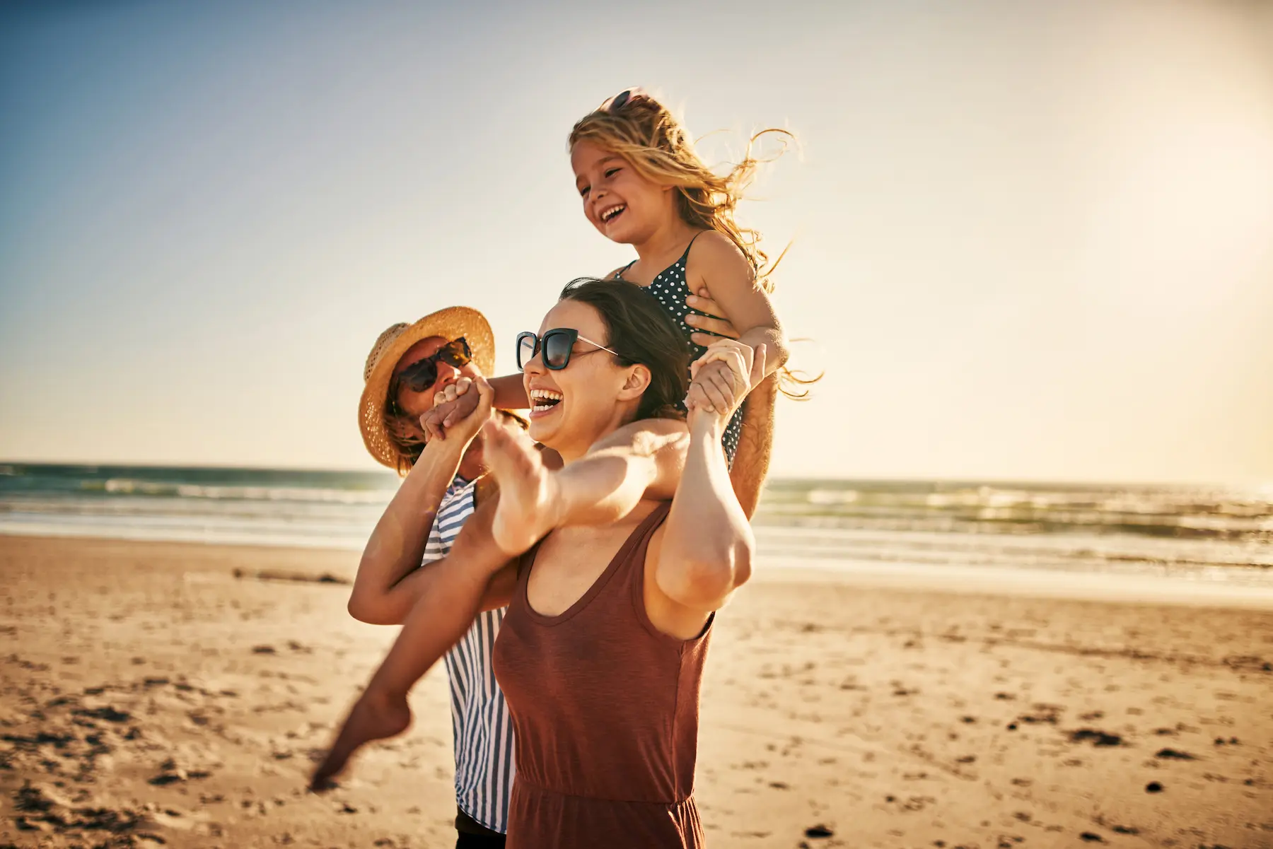 Fröhliche Familie spielt mit ihrem Kind am Strand bei Sonnenschein während eines Urlaubs am Meer