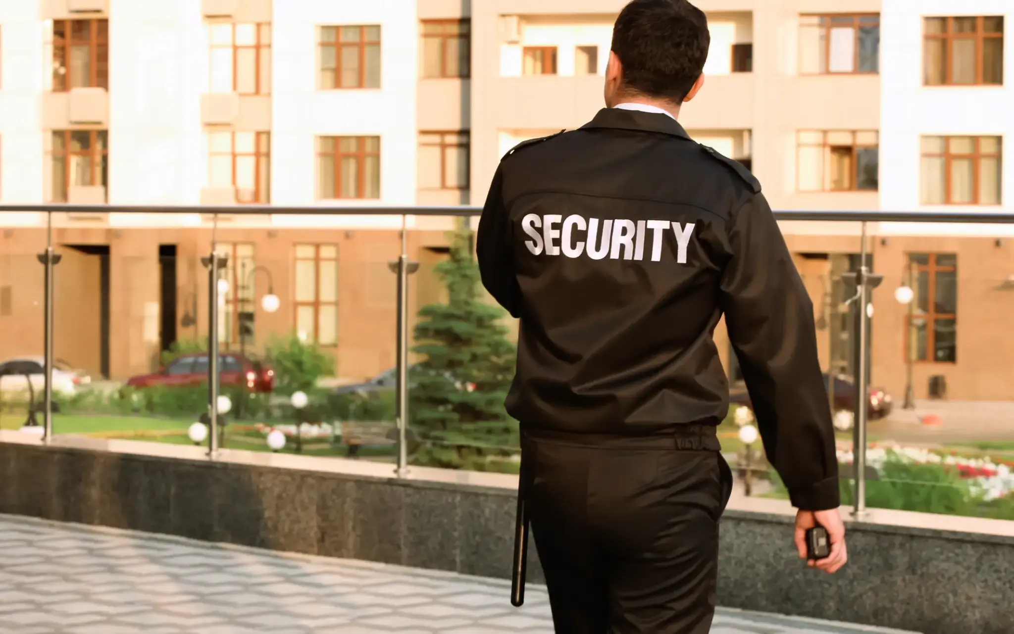 Security-Mitarbeiter im schwarzen Einsatzanzug mit Funkgerät bei Kontrollgang vor einem Wohn- oder Bürogebäude