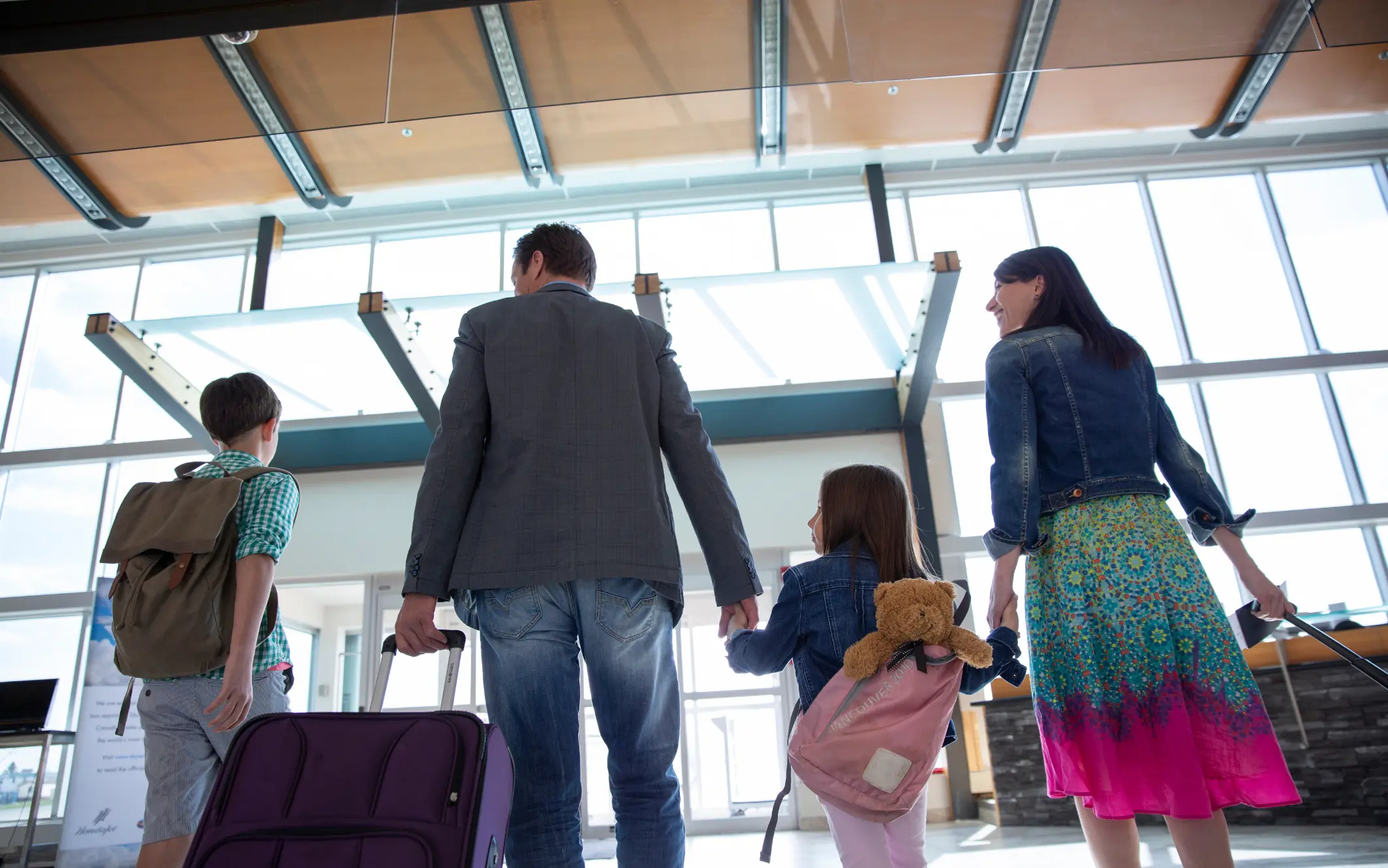 Familie mit zwei Kindern läuft mit Koffern durch einen hellen Flughafen auf dem Weg in den Urlaub