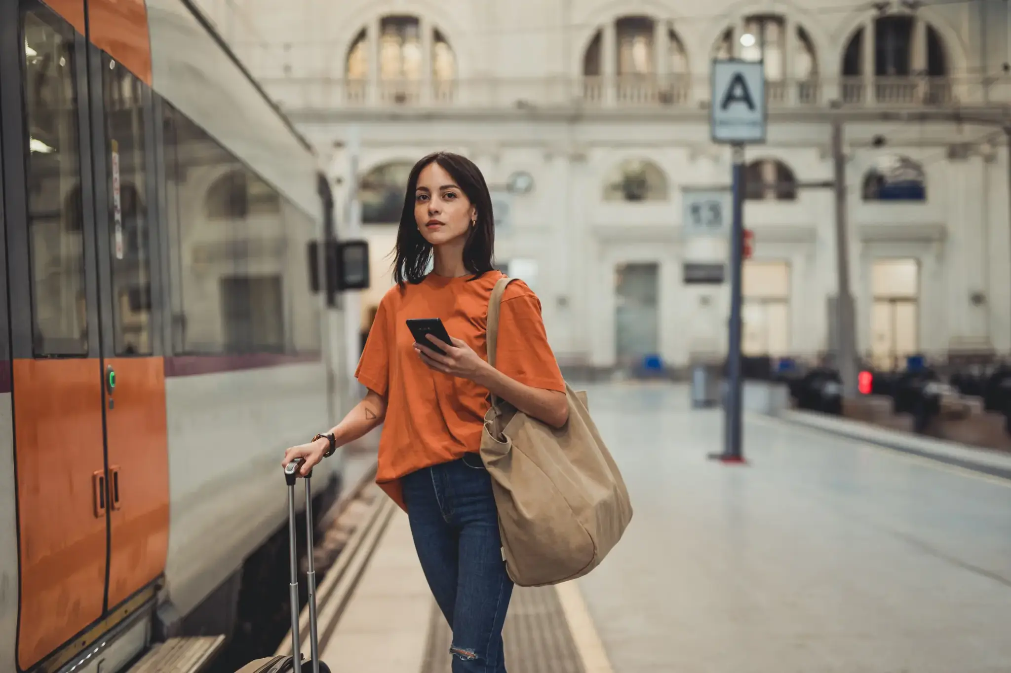 Junge Frau mit Koffer am Bahnsteig, blickt aufs Handy – Symbolbild für Flexibilität und Vorsorge mit Anwartschaftsversicherung