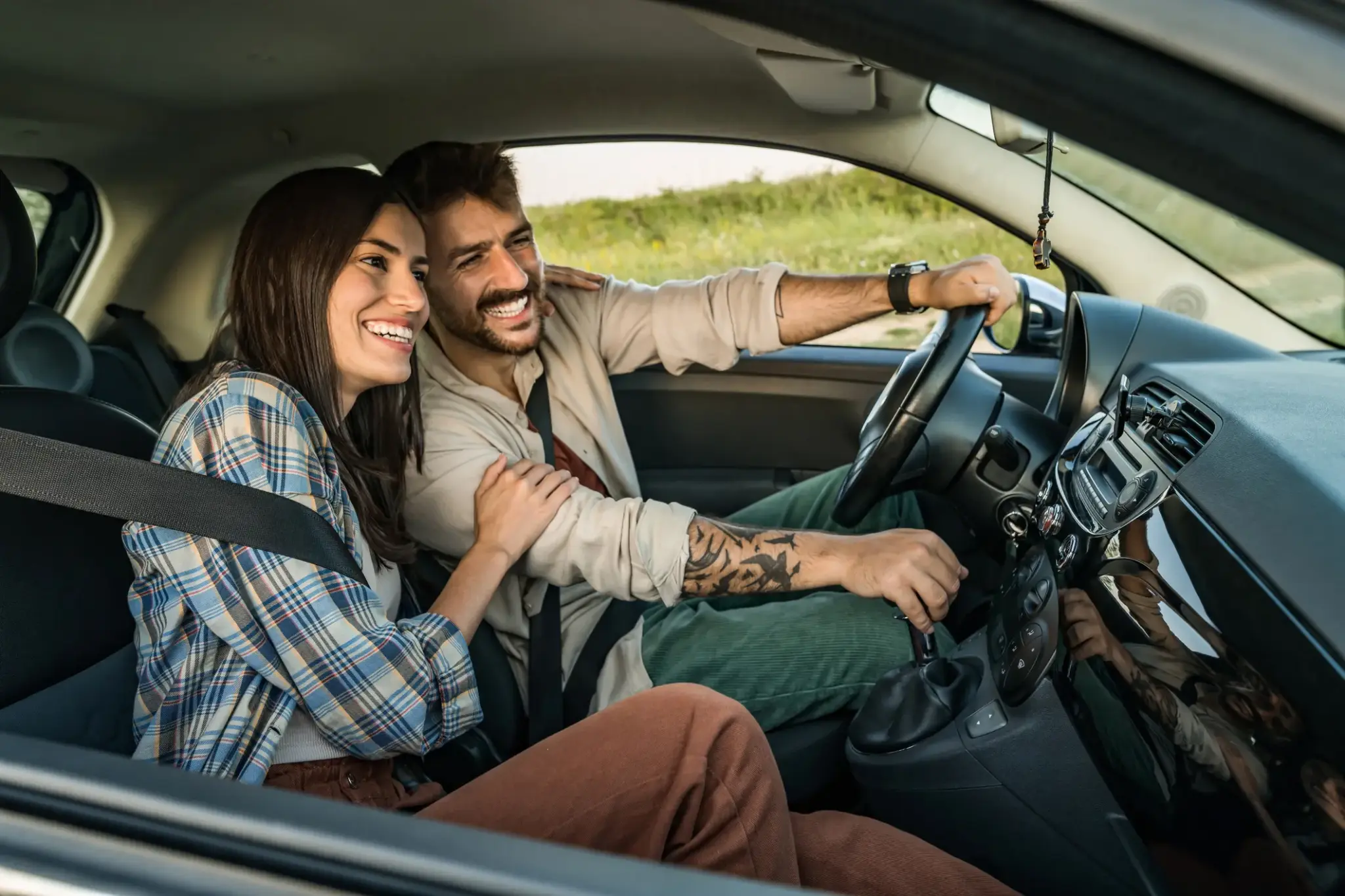 Junges Paar fährt lachend im Auto über eine Landstraße – Symbolbild für sichere und sorgenfreie Mobilität mit Autoversicherung