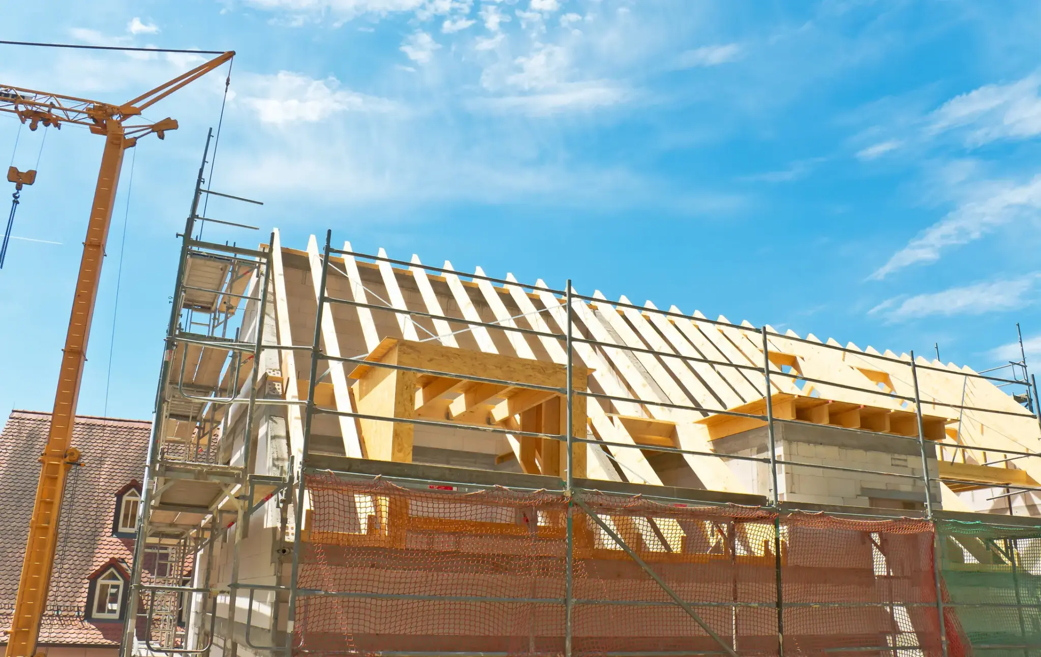 Wohnhaus im Rohbau mit Baugerüst und Kran bei sonnigem Wetter – Darstellung einer typischen Bauphase beim Hausbau.