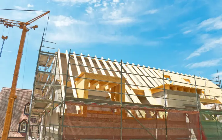 Wohnhaus im Rohbau mit Baugerüst und Kran bei sonnigem Wetter – Darstellung einer typischen Bauphase beim Hausbau.