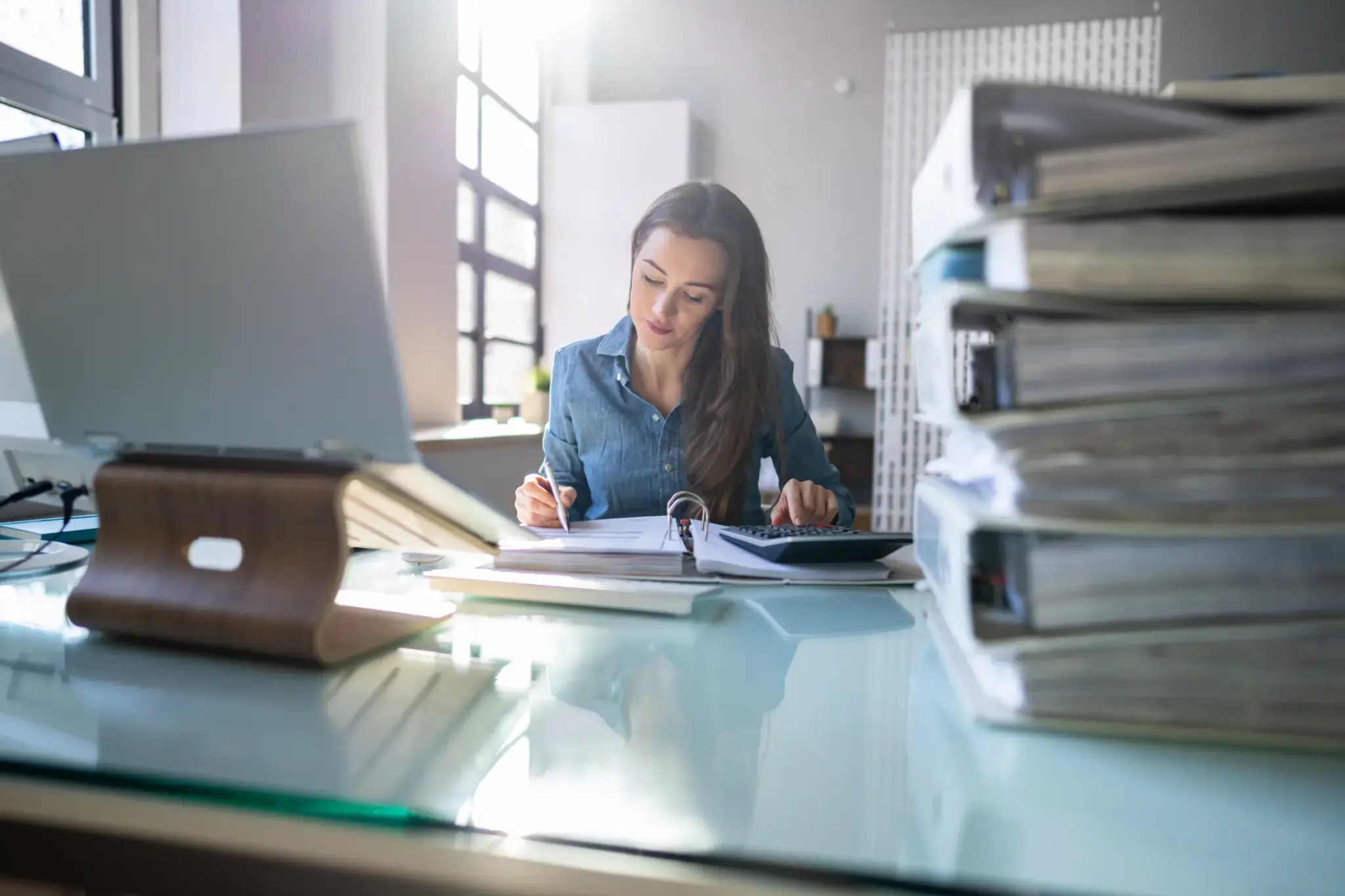 Dienstunfaehigkeitsversicherung | Junge Frau arbeitet konzentriert im Büro mit Akten und Laptop – Symbolbild für Dienstunfähigkeit und Absicherung im Beamtenberuf