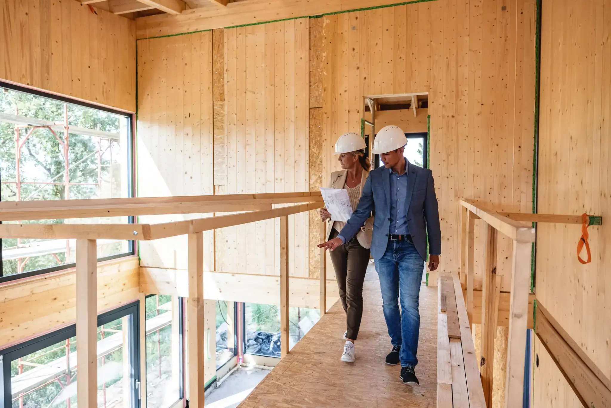 Feuerrohbauversicherung | Zwei Bauleiter mit Bauplänen und Helmen begehen einen Neubau aus Holz – Symbolbild für Feuerrohbauversicherung während der Bauphase.
