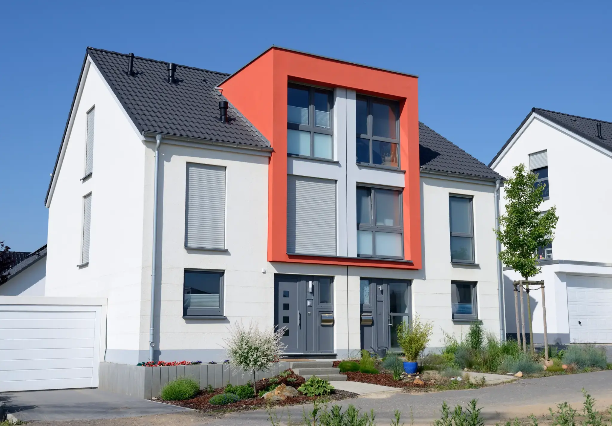 Gebaeudeversicherung Doppelhaushaelfte | Moderne Doppelhaushälfte mit weißer Fassade, grauem Dach und markantem orangenem Fassadenrahmen