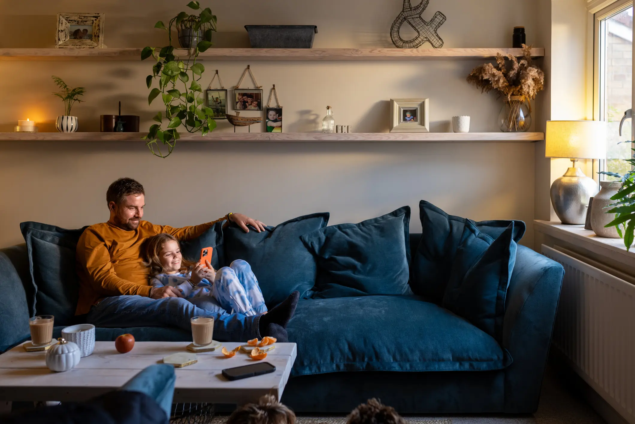 Vater und Tochter sitzen entspannt auf dem Sofa im Wohnzimmer und schauen gemeinsam auf ein Smartphone