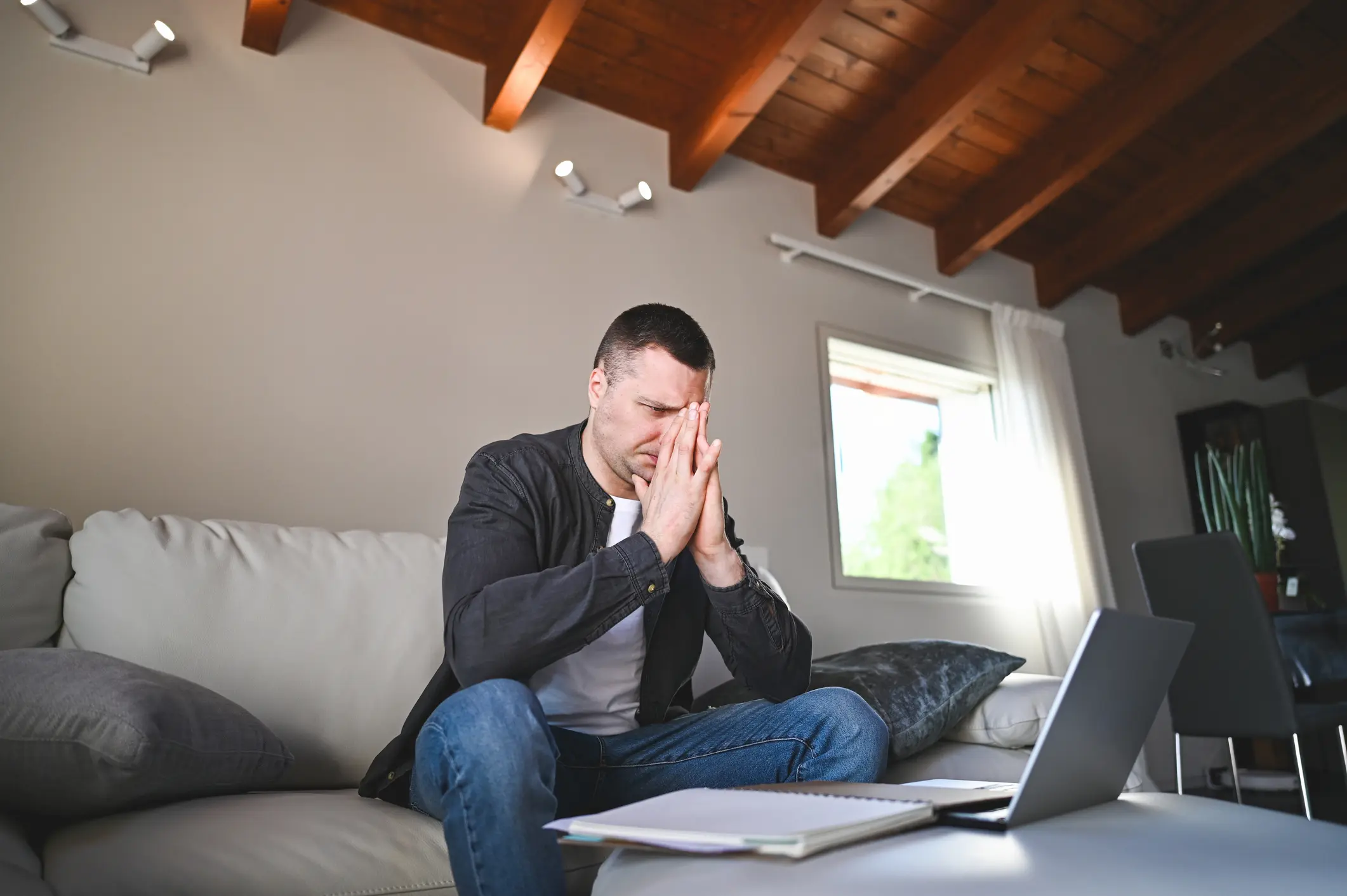 Mann sitzt frustriert auf dem Sofa in seiner Wohnung und blickt auf einen Laptop – symbolisch für finanziellen Stress durch Mietausfall.