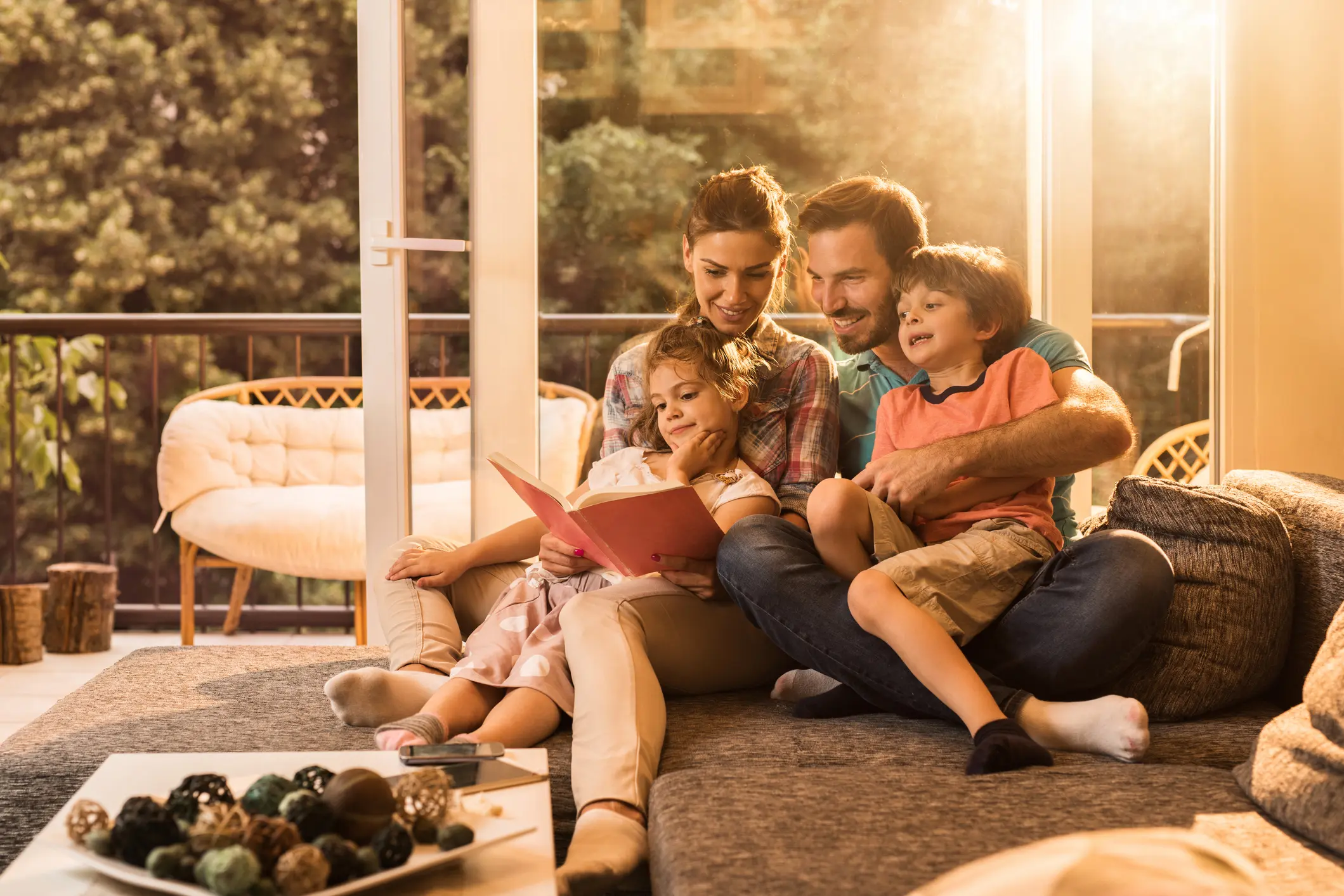 Glückliche Familie sitzt gemeinsam auf dem Sofa und liest – Symbolbild für Sicherheit durch sinnvolle Versicherungen