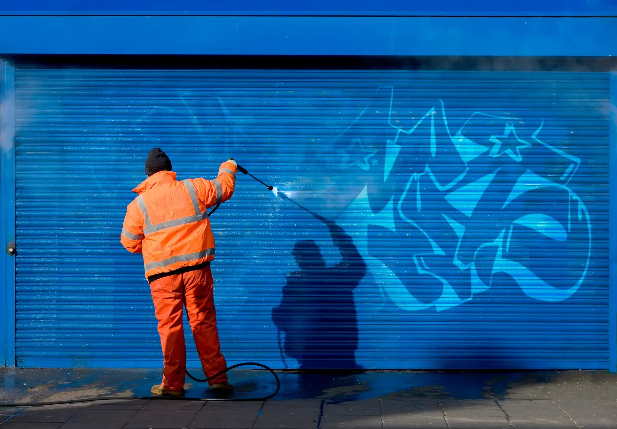 Mitarbeiter in Warnkleidung entfernt Graffiti von Garagentor – Reinigung nach Vandalismusschaden