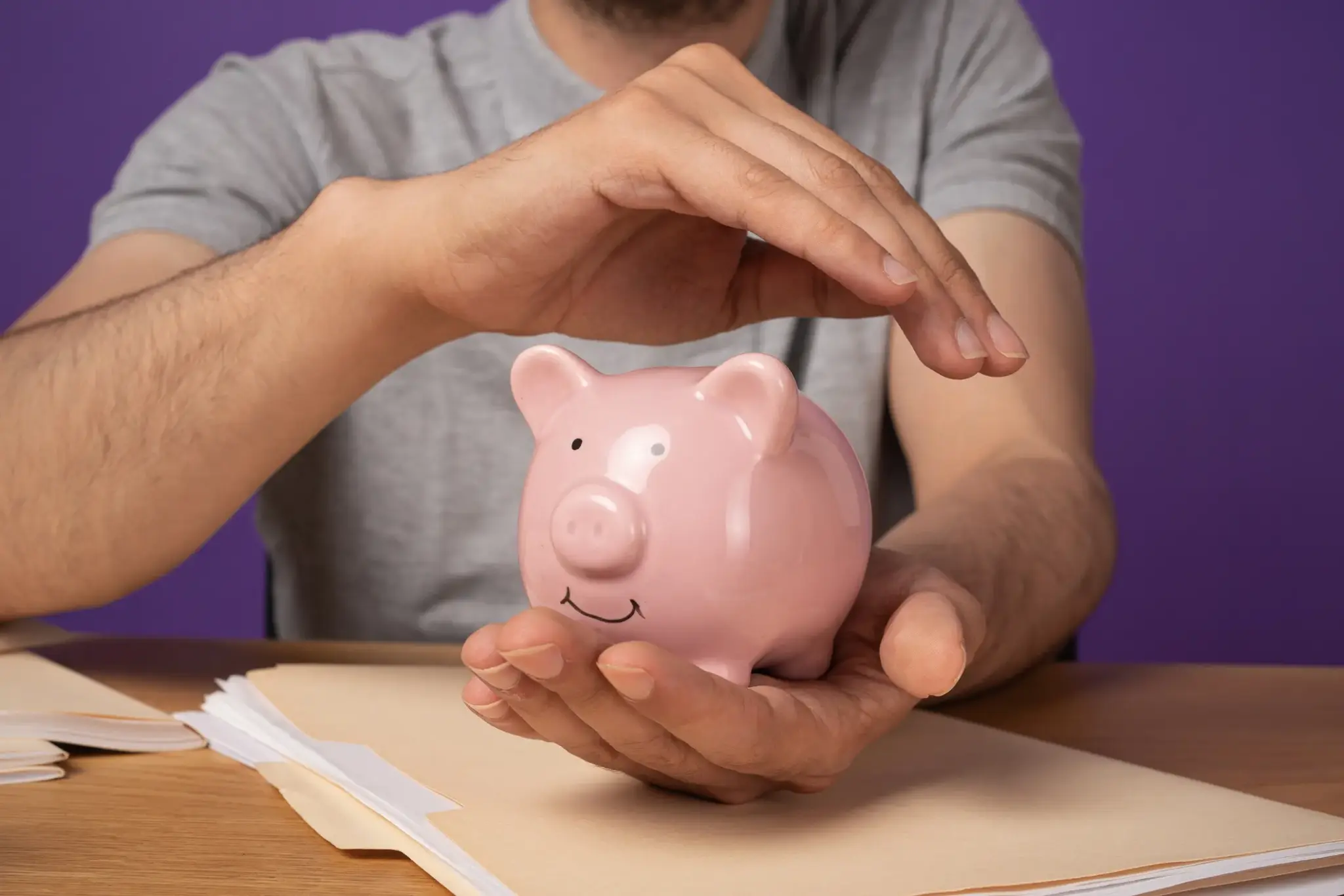 BU Altersvorsorge kombiniert | Mann schützt ein rosafarbenes Sparschwein mit seinen Händen – Symbol für finanzielle Sicherheit und kombinierte Vorsorge mit Berufsunfähigkeit.
