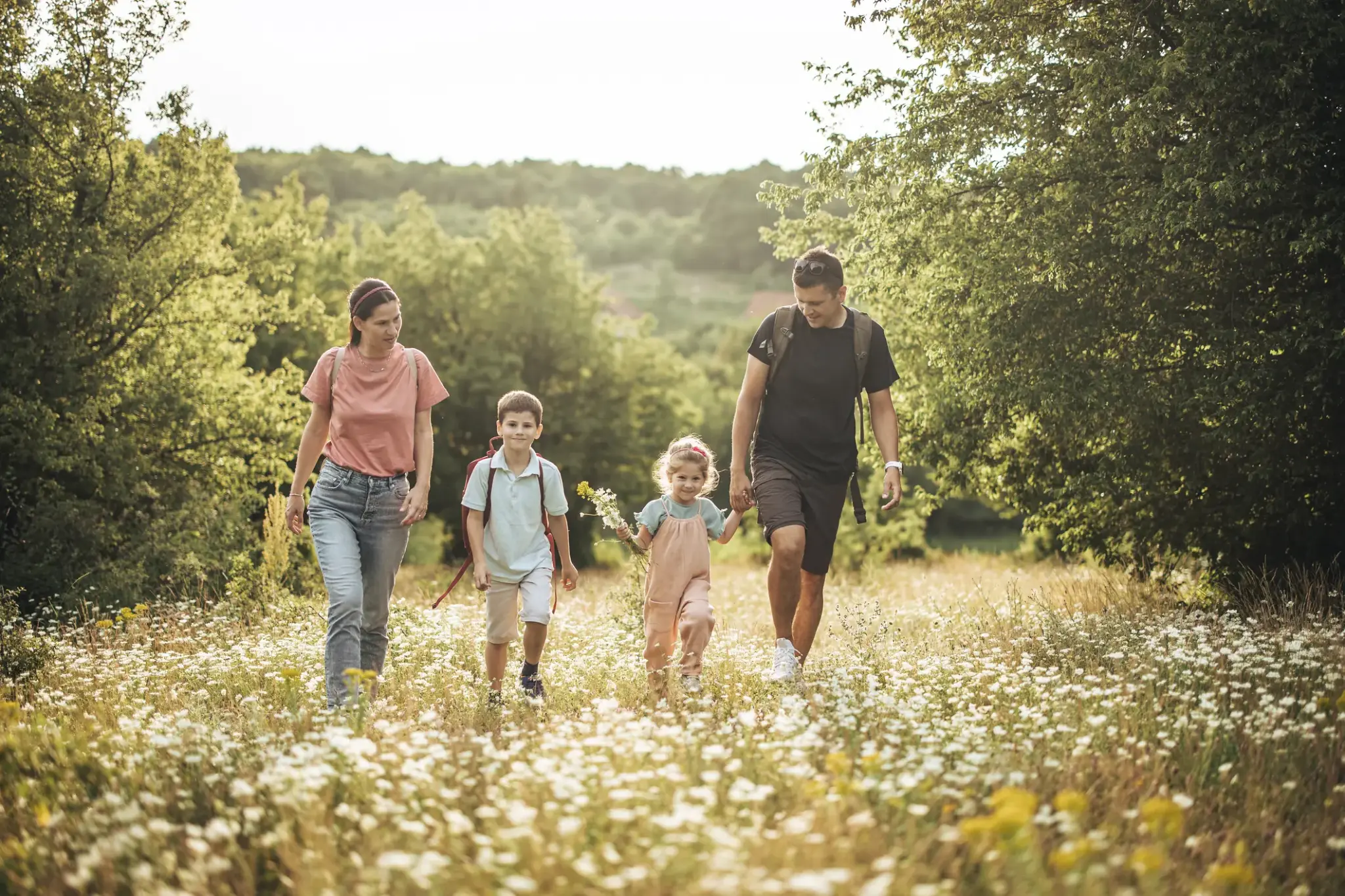 Eine junge Familie wandert gemeinsam durch eine Sommerwiese – Symbolbild für Freizeitaktivitäten und potenzielle Unfallrisiken im Alltag.