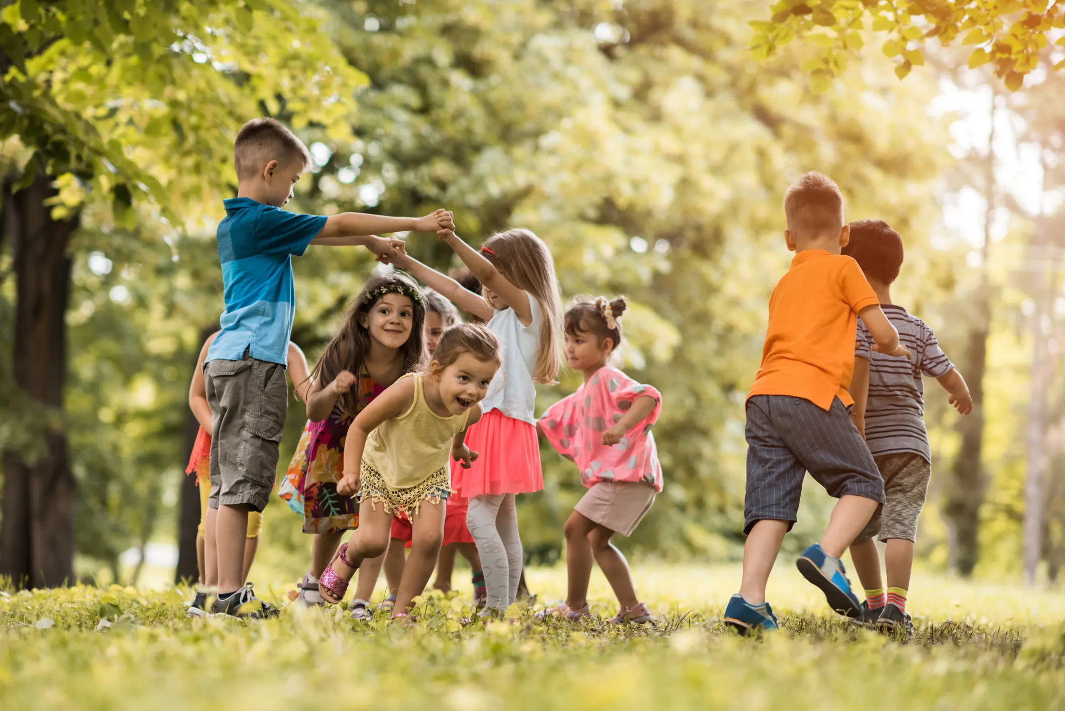 Fröhlich spielende Kinder im Park, die gemeinsam einen Kreis bilden – Symbol für Gesundheit, Bewegung und Unbeschwertheit.