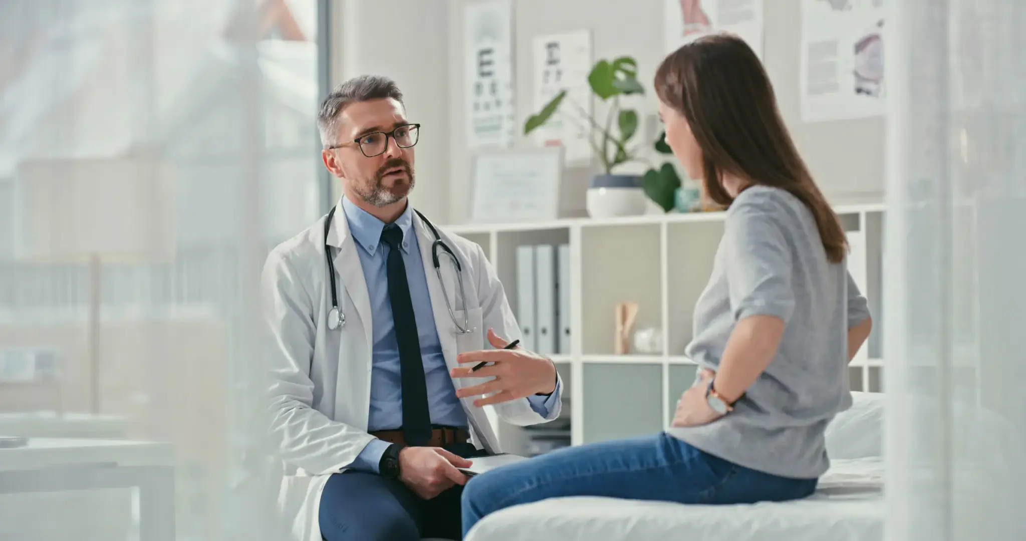 Impfschaden Unfallversicherung | Ein Arzt im weißen Kittel spricht mit einer Patientin im Behandlungsraum – Symbolbild für ärztliche Aufklärung nach Impfreaktion.