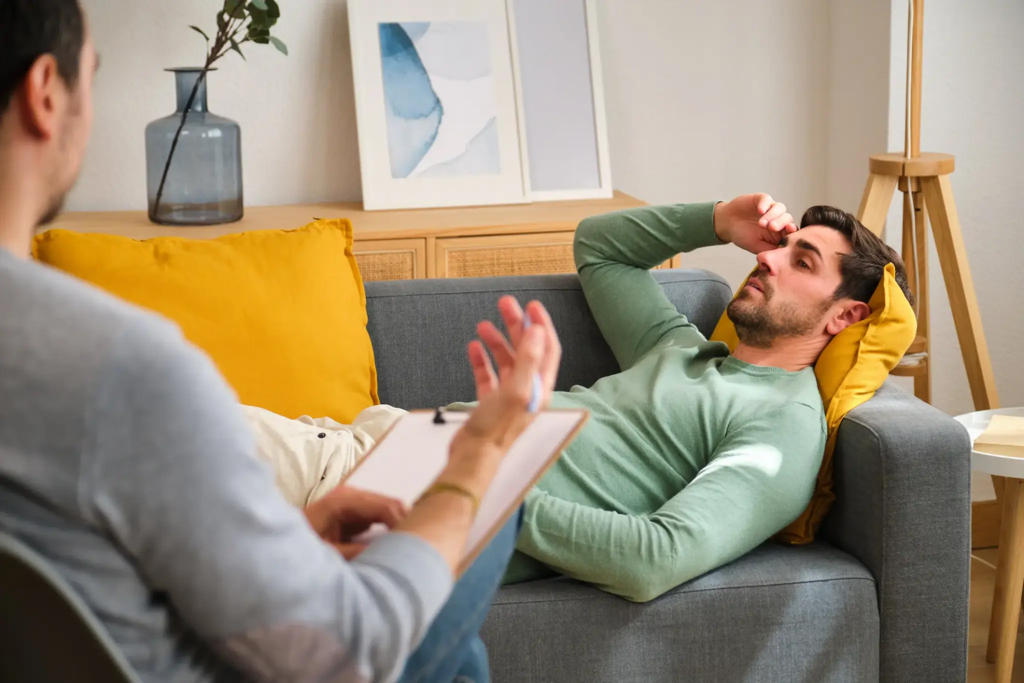 Ein Mann liegt erschöpft auf dem Sofa und spricht mit einem Therapeuten – Szene symbolisiert psychische Belastung im Leistungsfall BU.