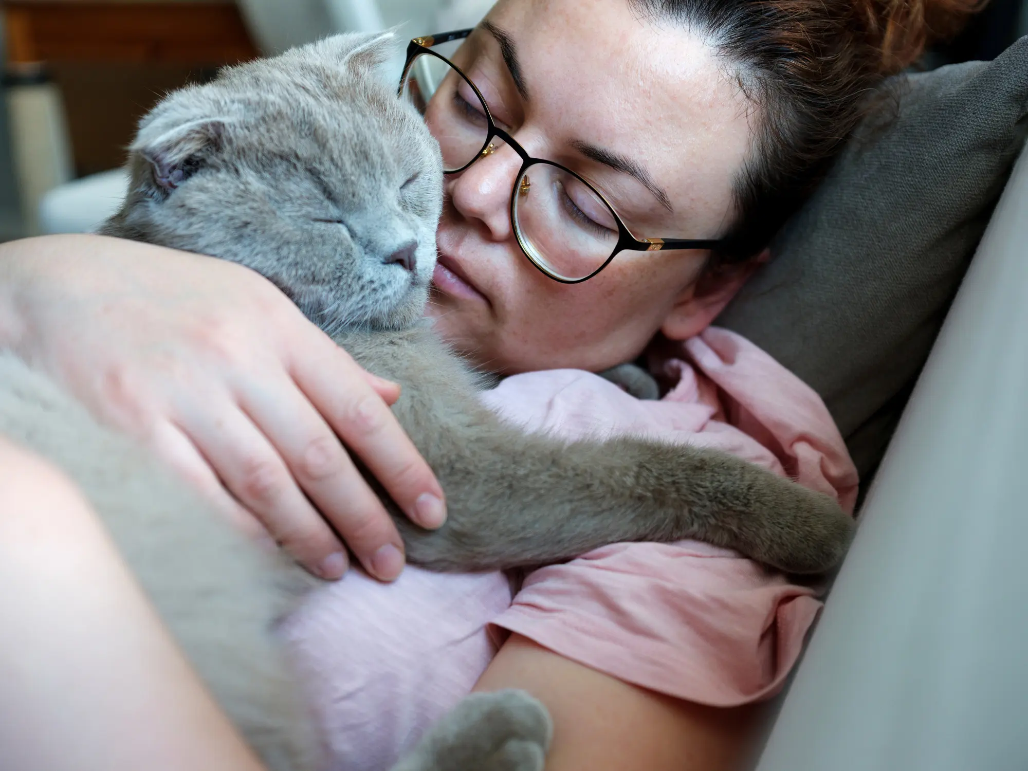 Eine Frau hält ihre kranke Katze liebevoll im Arm – beide liegen auf dem Sofa, eng aneinandergeschmiegt und in einem ruhigen Moment vereint.