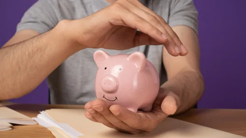 Mann schützt ein rosafarbenes Sparschwein mit seinen Händen – Symbol für finanzielle Sicherheit und kombinierte Vorsorge mit Berufsunfähigkeit.