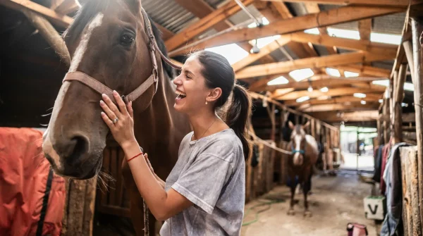 Junge Frau streichelt ihr Pferd im Stall – symbolisiert Vertrauen, Tierliebe und Verantwortung im pferdehaltenden Betrieb.