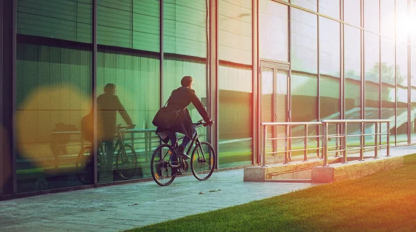 Ein Mann fährt mit dem Fahrrad zur Arbeit und nähert sich einem modernen Bürogebäude – Symbolbild für Dienstrad und nachhaltige Mobilität.