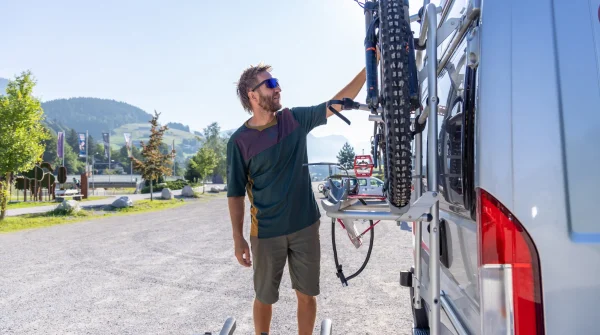 Mann befestigt ein Mountainbike auf einem Fahrradträger an einem Campervan