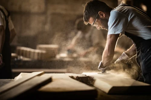 Handwerker beim Schleifen von Holz in einer staubigen Werkstatt