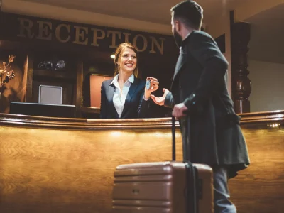 Rezeptionistin übergibt Hotelschlüssel an ankommenden Gast mit Koffer