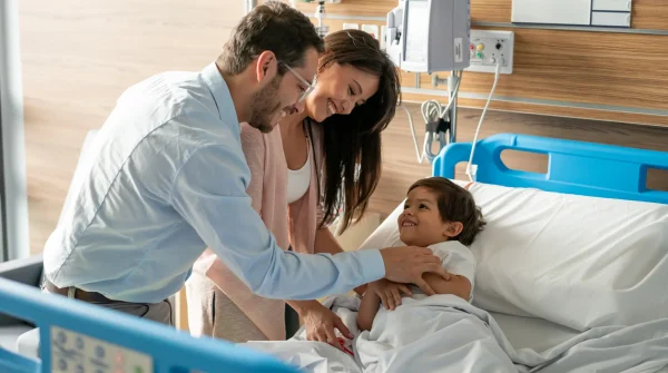 Eltern besuchen ihr lächelndes Kind im Krankenhausbett – Symbolbild für die Absicherung durch eine Zusatzversicherung