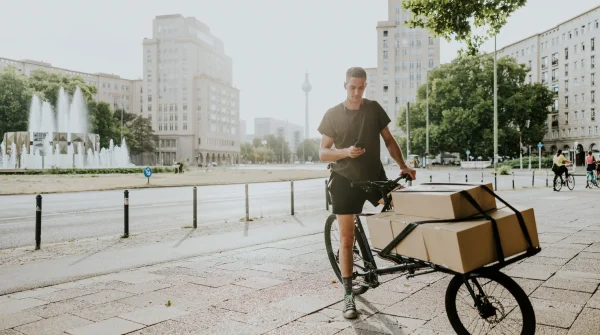 Ein junger Mann transportiert große Pakete auf einem Lastenrad durch die Stadt – nachhaltige Lieferung im urbanen Raum.