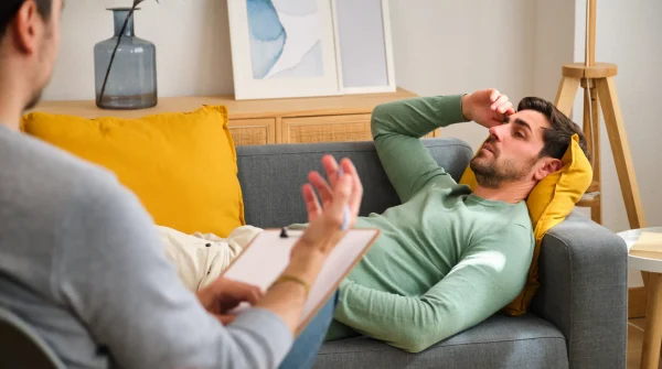 Ein Mann liegt erschöpft auf dem Sofa und spricht mit einem Therapeuten – Szene symbolisiert psychische Belastung im Leistungsfall BU.