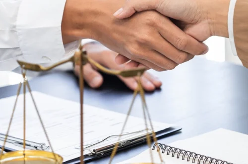 Zwei Personen geben sich die Hand neben Justiz-Symbolen – Rechtsschutzvereinbarung und juristische Absicherung im Fokus