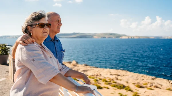Älteres Paar steht am Meer auf einer Promenade – Symbolbild für Rente im Ausland und Lebensabend in Südeuropa