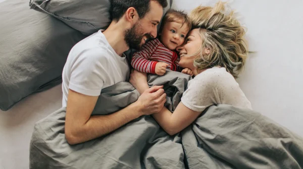 Junge Familie liegt lachend im Bett mit Baby – Symbolbild für Schutz und finanzielle Absicherung durch Risikolebensversicherung