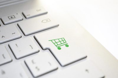 Computertastatur mit einem Einkaufswagen darauf, symbolisiert Online-Shop-Versicherungen, die den sicheren und reibungslosen Ablauf von E-Commerce-Aktivitäten gewährleisten.