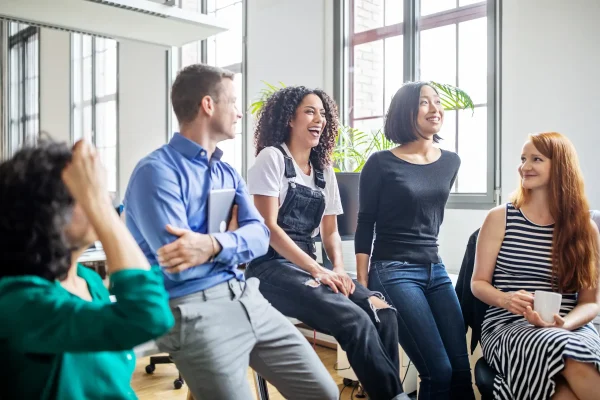 Junge Angestellte sitzen in einem modernen Büro zusammen, lachen und unterhalten sich in entspannter Atmosphäre